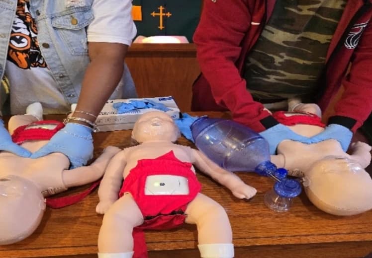 Students practicing infant CPR on manikins with a bag valve mask during a Two Breaths Away training session